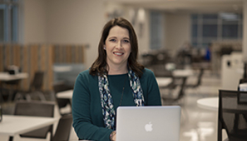 Young woman dressed in blue sits behind a laptop at a table