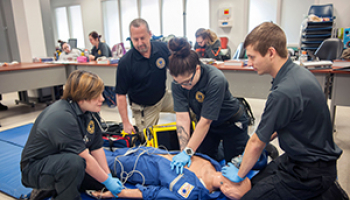 A group of EMS students practice on a simulation mannequin while their instructor observes