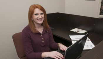 A young woman smiles while typing on a laptop