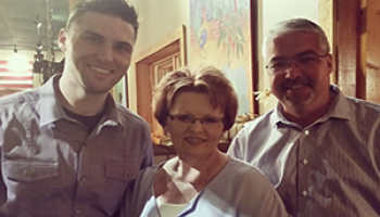A woman smiles as she stands in between her son and husband.