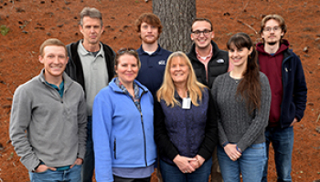 A group of people huddle together underneath a tree on a cold winter day.