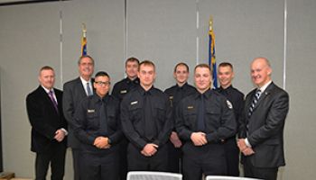 A group of law enforcement graduates huddle close in their uniforms beside administration members.