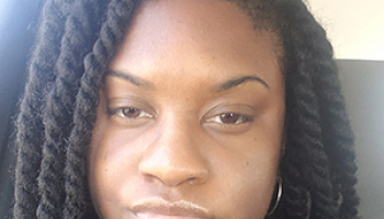 A young woman in a navy sweater smiles in a selfie.