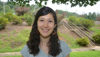 A young woman with black hair smiles under a tree on a foggy morning