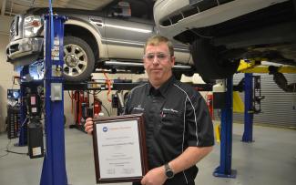 Man holds plaque in garage with cars on lifts in background.