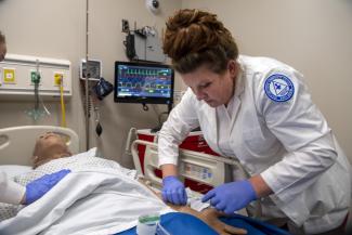 Female student inserts an IV into arm of a simulation mannequin