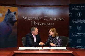 Dr. Brown &amp; Dr. Tomas shake hands at a board room table..