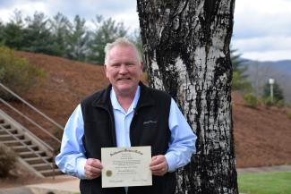 man poses outdoors with diploma