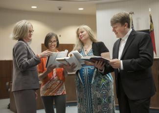 Female attorney stands with her students in a local court room reading legal books.