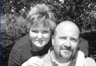A woman lovingly leans over her husband with her hands placed on his shoulders.